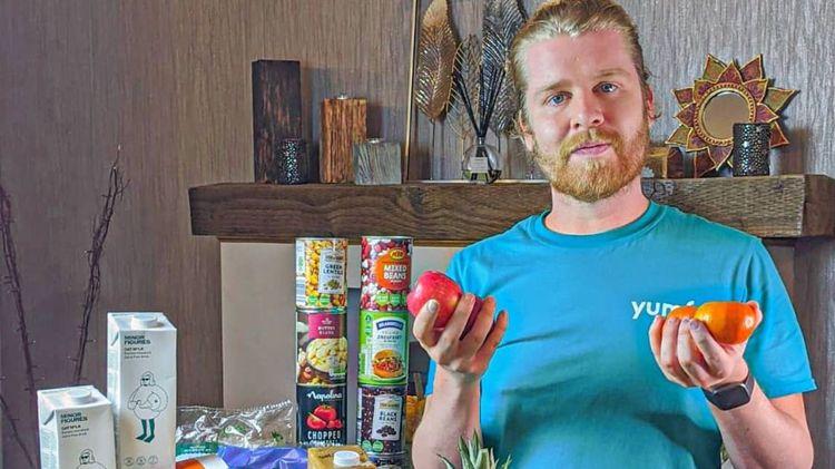  Plant-based nutritionist Callum Weir holding vegetables and next to canned vegan foods 